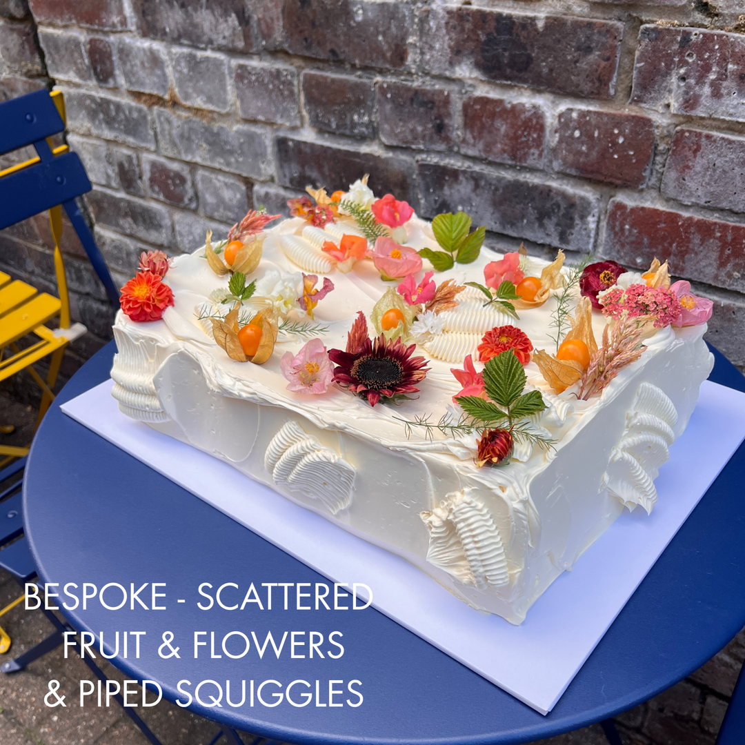 A rectangular white frosted cake decorated with scattered fruit, flowers, and piped squiggles. London